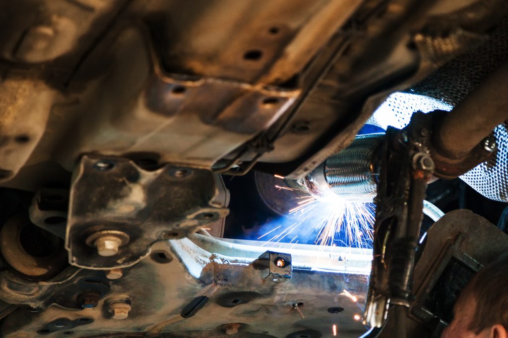 welder welds silencer on car by argon welding
